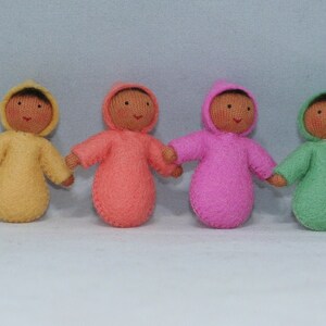 Puede incluir: Siete mu&ntilde;ecas de fieltro que llevan atuendos con capucha de varios colores, entre ellos blanco, amarillo, rosa, naranja, verde y azul. Las mu&ntilde;ecas tienen caras marrones y todas llevan el mismo estilo de atuendo con capucha.