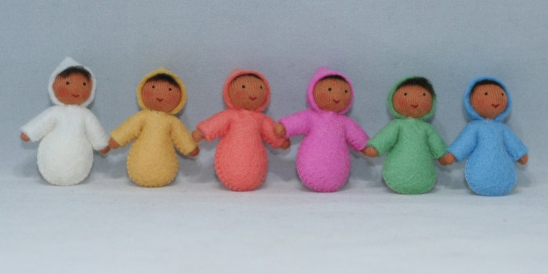 Puede incluir: Siete mu&ntilde;ecas de fieltro que llevan atuendos con capucha de varios colores, entre ellos blanco, amarillo, rosa, naranja, verde y azul. Las mu&ntilde;ecas tienen caras marrones y todas llevan el mismo estilo de atuendo con capucha.