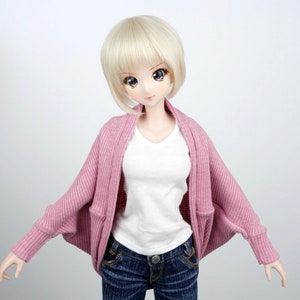 Op de afbeelding: Een roze gebreide cardigan met lange mouwen en een losse pasvorm. De cardigan heeft een V-hals en wordt gedragen over een wit T-shirt en een blauwe jeans.
