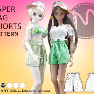 Peut inclure: Deux poupées portant des shorts en papier. La poupée de gauche porte un short vert clair avec une ceinture marron. La poupée de droite porte un short vert vif avec une ceinture verte. Les deux poupées portent des hauts blancs. L'image comprend un patron pour faire des shorts en papier.