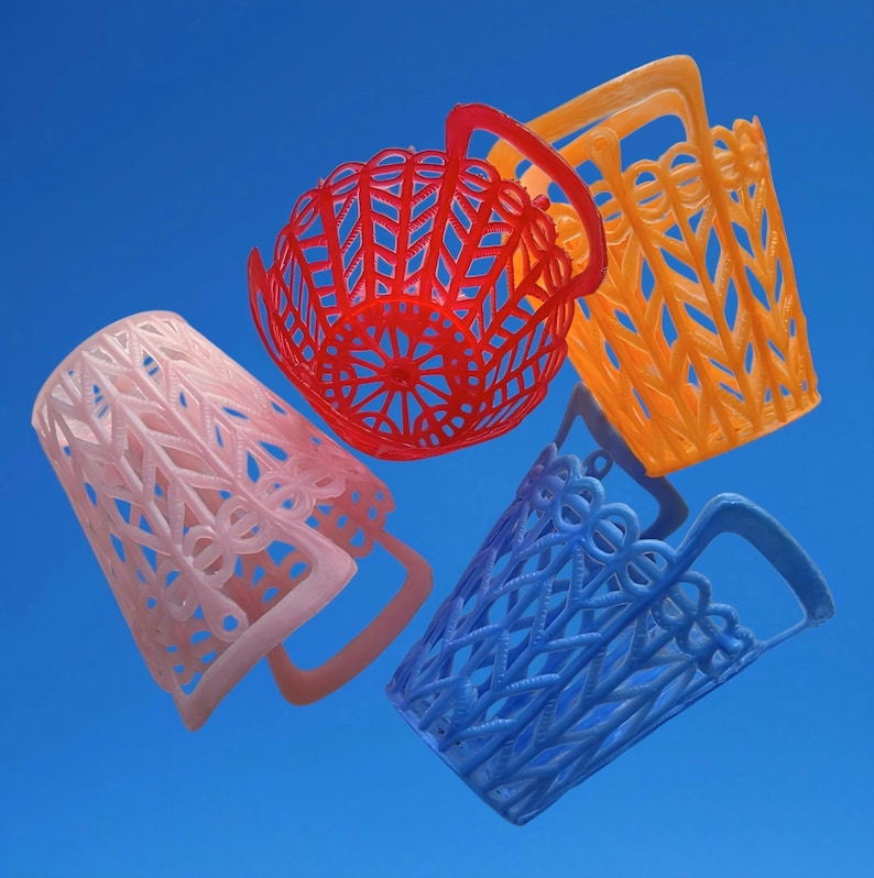 May include: Four brightly coloured, openwork baskets in pink, red, orange, and blue against a blue background. Each basket has a handle and a unique geometric or floral design, showcasing a variety of textures and patterns.