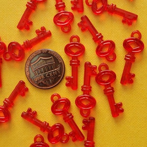 May include: A collection of red plastic toy keys on a yellow background. The keys are all different sizes and shapes, and some have a small loop at the top. There is a US penny in the center of the image.