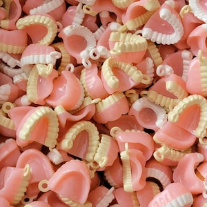 May include: A pile of pink and white plastic dentures. The dentures are all different sizes and shapes, and some have teeth.