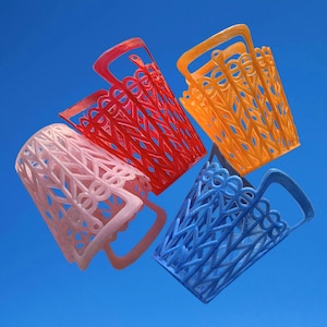 May include: Four brightly coloured, openwork baskets in pink, red, orange, and blue against a blue sky. Each basket has a handle and a decorative, geometric pattern. The baskets appear to be made of plastic.