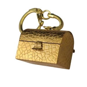 May include: A small, gold-colored treasure chest keychain. The miniature chest has a textured surface and a clasp closure. The keychain includes a ring and a decorative, curved handle.