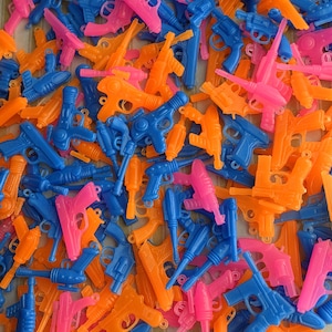 May include: A collection of colorful toy guns in blue, pink, and orange. The assortment includes various styles of plastic pistols and water guns, creating a playful and vibrant display.