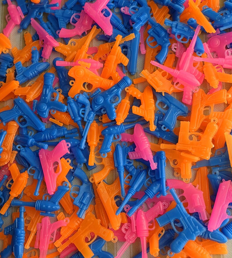 May include: A collection of colorful toy guns in blue, pink, and orange. The assortment includes various styles of plastic pistols and water guns, creating a playful and vibrant display.