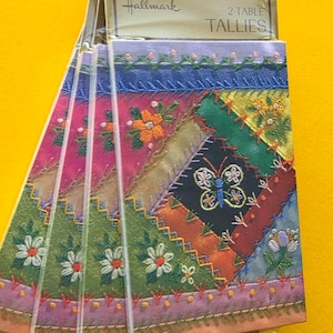 May include: A stack of eight Hallmark 2-Table Tallies. Each tally features a colorful patchwork design with embroidered flowers and a butterfly. The top of the stack is labeled with the Hallmark logo and the words "EIGHT" and "2-TABLE TALLIES".