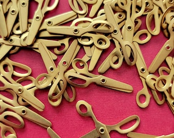 May include: A collection of small, gold-colored metal scissor-shaped charms scattered across a solid pink surface. Each charm features a simple silhouette with two finger loops and a central pivot point, creating a uniform pattern.