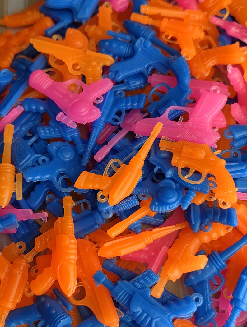 May include: A pile of colorful toy water guns in shades of blue, orange, and pink. The plastic guns vary in style, including pistols and rifles. The image is a close-up, showing the details of the toys.