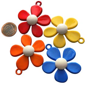May include: Four colorful flower-shaped charms in red, yellow, orange, and blue, each with a white center and a loop for hanging. A penny is included for size reference. These charms are suitable for jewelry making or craft projects.