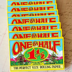 May include: A stack of yellow and blue rolling paper packs with the text "ONE & HALF 1 1/2 THE PERFECT SIZE ROLLING PAPER" printed on the front.