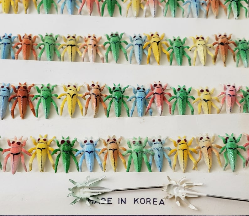 May include: Rows of colorful, miniature insect figurines in various colors, including green, yellow, orange, and blue. Each insect has a detailed design with tiny legs and antennae. The text "MADE IN KOREA" is visible at the bottom.