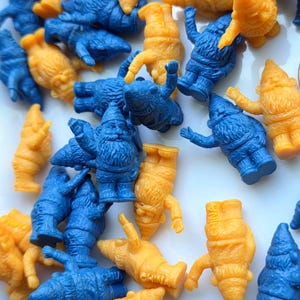 May include: A collection of small, plastic gnome figurines in blue and orange. The gnomes are in various poses, some standing and some lying down. The image is taken from a top-down perspective, with the gnomes scattered across the surface.