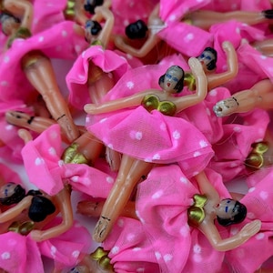 May include: A collection of small plastic ballerina figurines. Each figurine is dressed in a pink tutu with white polka dots and a gold bodice. The ballerinas have black hair and are posed in various ballet positions.