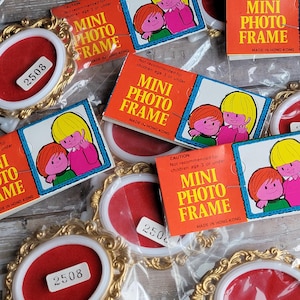 May include: A collection of vintage mini photo frames and packaging. The frames have a gold-colored ornate design with a red oval center. The packaging is orange with the text "MINI PHOTO FRAME" and a cartoon illustration.