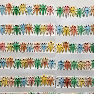 May include: A display of colorful insect-shaped stick pins. The pins are arranged in rows on white cards, with each insect featuring a different color, including green, yellow, blue, orange, and pink. The text "Pet Stick Pins" is at the top.