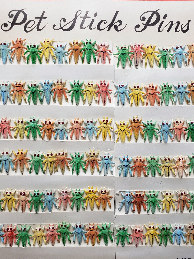May include: A display of colorful insect-shaped stick pins. The pins are arranged in rows on white cards, with each insect featuring a different color, including green, yellow, blue, orange, and pink. The text "Pet Stick Pins" is at the top.