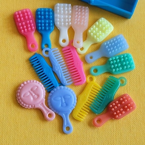 May include: A collection of colorful miniature doll accessories, including combs and brushes in various shades of pink, blue, white, yellow, green, and orange. Two small hand mirrors with faces are also present. The items are arranged on a yellow surface.