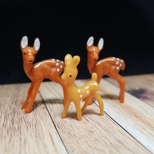 May include: Three plastic toy deer figurines. Two are brown with white spots and one is yellow with white spots.