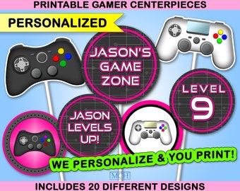 May include: Printable gamer themed party centerpieces with a pink and black color scheme. The centerpieces feature a variety of designs including a video game controller, a level 9 sign, and the text "Jason's Game Zone" and "Jason Levels Up!"