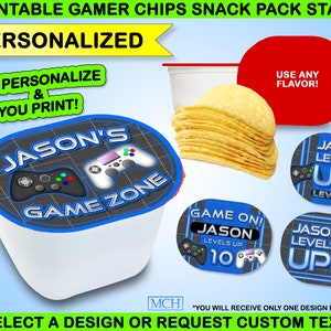 May include: A white snack cup with a personalized lid featuring a video game controller design and the text "JASON'S GAME ZONE." Additional designs include "GAME ON! JASON LEVELS UP 10" and "JASON LEVELS UP! LEVEL 10." The image also shows a stack of chips.