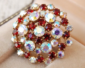 Peut inclure: Une broche ronde avec des strass rouges et clairs irisés sertis dans un métal doré.
