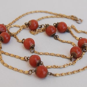 Può includere: Una collana a catena d'oro con più fili e perline rotonde arancioni.