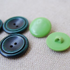Peut inclure: Quatre boutons, deux verts et deux vert foncé avec un motif marbré. Les boutons verts sont ronds et lisses, tandis que les boutons vert foncé ont deux trous.