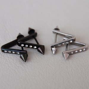 May include: Two pairs of triangle-shaped earrings with pointed ends. One pair is black with clear rhinestones, and the other pair is silver with clear rhinestones.