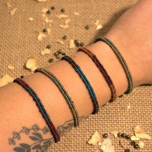 Könnte beinhalten: Ein Set aus sechs geflochtenen Armbändern in verschiedenen Grüntönen, Braun- und Blautönen. Die Armbänder sind auf dem Handgelenk einer Person gestapelt.
