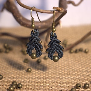 Peut inclure: Une paire de boucles d'oreilles en macramé bleu foncé avec des perles dorées et une forme de goutte.