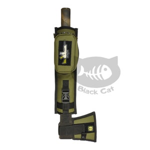 May include: A green and black axe sheath with a small pocket on the front. The pocket has a black and white graphic of a rifle. The sheath has a black strap and buckle. The sheath is attached to a green and black axe head.