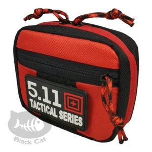 May include: A red and black tactical pouch featuring a rectangular black patch with the white text 5.11 TACTICAL SERIES and a red square logo. The pouch has a zippered closure with red and black cord pulls at the top and side, constructed from a durable, textured fabric material.