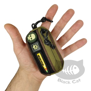 May include: A small, green and brown zippered pouch with a black zipper pull. The pouch has three patches attached to it: a skull, a paw print, and a yellow and orange bullet with the text "Run Like F*#% All" on it.