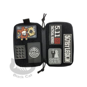 May include: Black tactical pouch with multiple patches. Patches include a skull jester with a playing card, a geometric design, a target, the text "5.11 Tactical Series", and the text "501st Legion". The pouch is open, revealing a zippered interior.