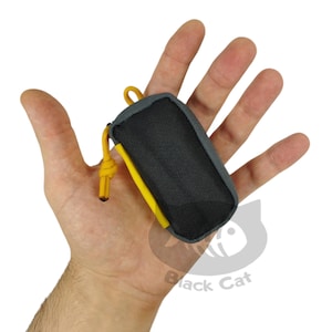 May include: A small grey pouch with a yellow zipper pull and a black drawstring. The pouch is made of a soft, textured fabric.