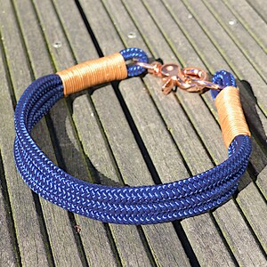 Puede incluir: Un collar de perro de cuerda azul marino con un cierre de oro rosa y detalles de cuero marrón.