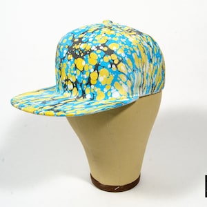 May include: A blue, yellow and black patterned baseball cap with a curved brim. The cap is on a tan mannequin head.