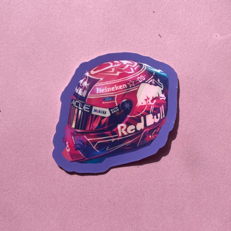 May include: A sticker featuring a Red Bull racing helmet design. The helmet is primarily red with white and blue accents, and includes the Red Bull logo, the word "Heineken", and other sponsor logos. The sticker has a purple border.