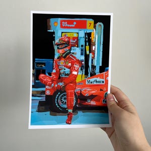 May include: A red race car with a driver wearing a red racing suit and helmet. The car is parked at a gas station with a Shell V-Power sign. The car has the word "Marlboro" on the side.