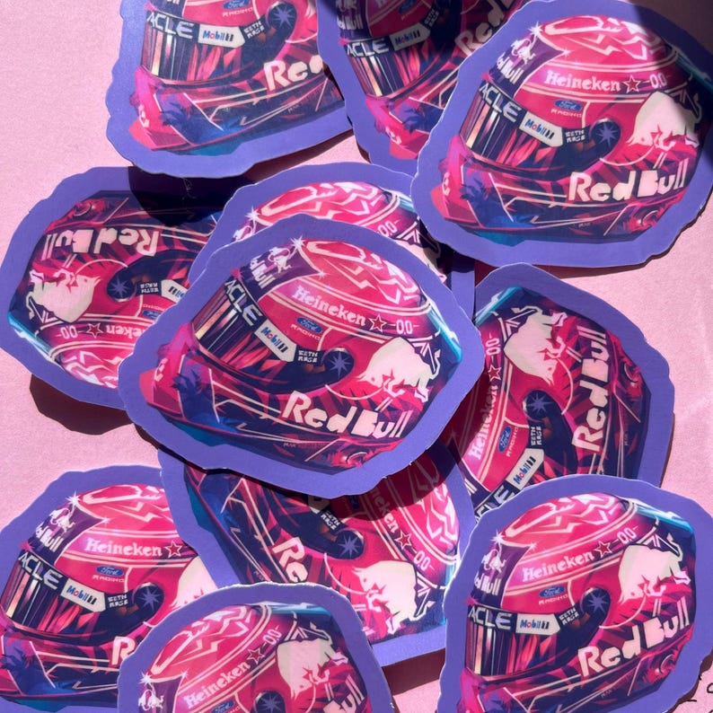 May include: A collection of stickers featuring a racing helmet design. The stickers have a purple border and a red, pink, and blue color scheme. The Red Bull logo and the word "Heineken" are visible on the helmet.