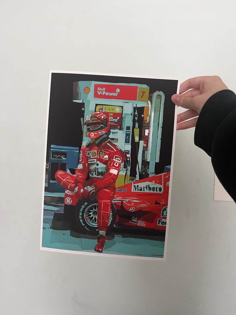 May include: A red Formula One race car with the Marlboro logo on the side. A race car driver wearing a red racing suit and helmet is sitting on the car. The car is parked at a gas station with a Shell V-Power sign.