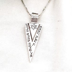 May include: A silver necklace with a pendant shaped like a triangle. The pendant has a Star of David in the center and Hebrew text around the edges.