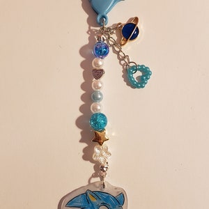 May include: A blue and white beaded keychain with a blue and gold planet charm, a blue heart charm, and a blue and white Sonic the Hedgehog charm.