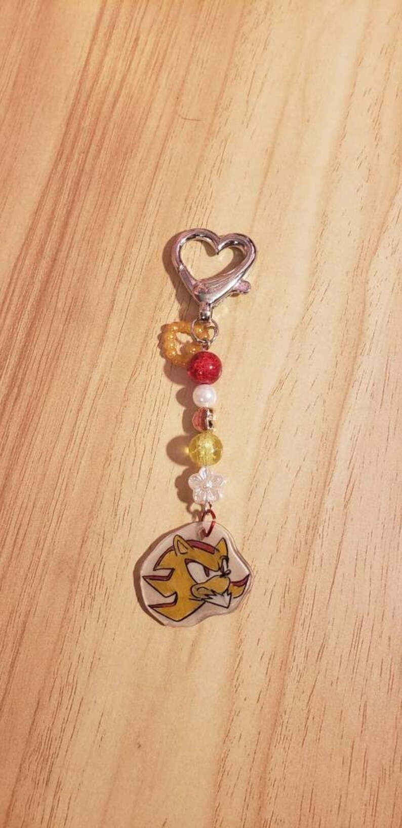 May include: A silver heart-shaped keychain with a red, white, and yellow beaded charm featuring a cartoon character with a yellow and red design.
