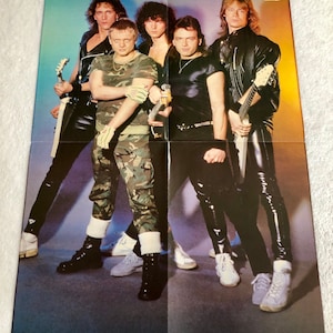 May include: A promotional poster for the German rock band Accept. The poster features a photo of the band members in a studio setting. The band members are wearing leather jackets and jeans. The poster is printed in color and has a glossy finish.