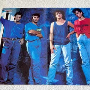 Può includere: Un poster con quattro uomini in una band. Gli uomini indossano jeans blu e camicie casual. Il poster ha uno sfondo blu con motivi bianchi e blu.