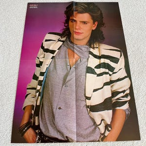 Puede incluir: Una chaqueta de rayas blancas y negras con una camisa gris debajo. La persona lleva un cinturón negro y tiene el pelo largo y oscuro.