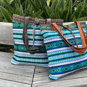 May include: Two tote bags with colorful geometric patterns and leather straps. The bags are made of fabric and have a woven design. The bags are sitting on a wooden bench.